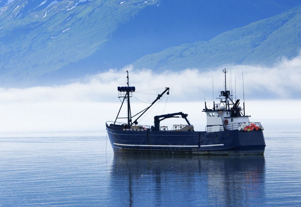 A deep blue fishing trawler at anchor on a calm misty sea